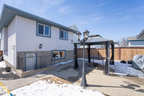 Rear exterior featuring light-colored siding with blue trim, a lower-level entry door with security bars, and a ground-level window - 1904 36 Avenue, Edmonton, AB - Outdoor With Exterior