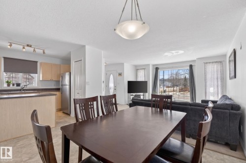 Open-concept living space featuring a dining area with a contemporary ceiling light fixture, kitchen with light wood cabinetry and stainless steel appliances, and a living room with a large window - 1904 36 Avenue, Edmonton, AB - Indoor Photo Showing Dining Room