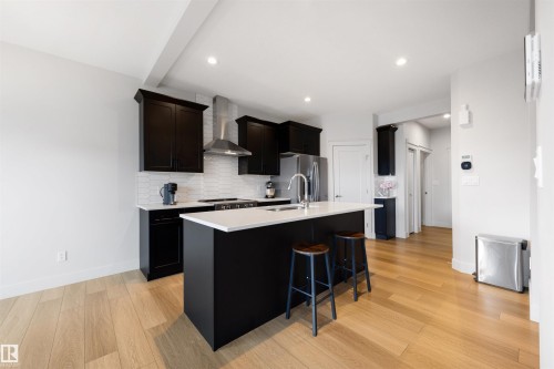 Modern kitchen featuring a central island with countertop seating, dark cabinetry, and light wood-finish flooring - 3193 Checknita Way, Edmonton, AB - Indoor Photo Showing Kitchen With Upgraded Kitchen