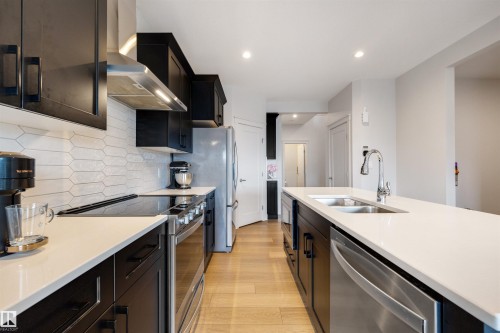 Contemporary kitchen featuring light wood-finish flooring, dark cabinetry, and light countertops - 3193 Checknita Way, Edmonton, AB - Indoor Photo Showing Kitchen With Stainless Steel Kitchen With Double Sink With Upgraded Kitchen