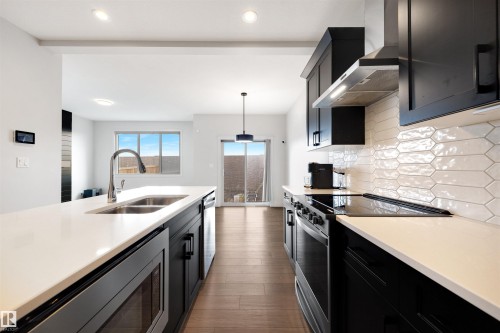 Contemporary kitchen featuring sleek black cabinetry, light countertops, and wood-finish flooring - 3193 Checknita Way, Edmonton, AB - Indoor Photo Showing Kitchen With Double Sink With Upgraded Kitchen