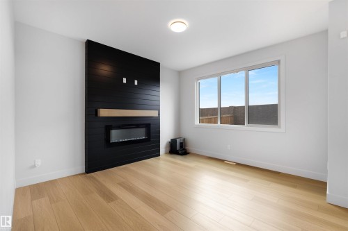 Modern living area featuring a shiplap accent wall with an electric fireplace and wood-finish mantel - 3193 Checknita Way, Edmonton, AB - Indoor Photo Showing Living Room With Fireplace