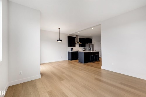 Open-concept interior featuring light wood-finish flooring, white walls, and a modern black pendant light fixture - 3193 Checknita Way, Edmonton, AB - Indoor