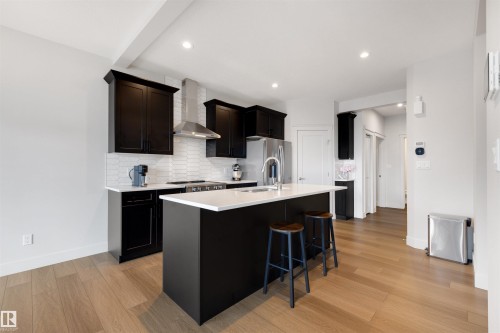 Modern kitchen featuring black cabinetry, white countertops, stainless steel appliances, and a central island with bar seating - 3193 Checknita Way, Edmonton, AB - Indoor Photo Showing Kitchen With Upgraded Kitchen