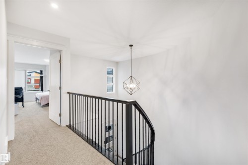 Upper-level landing featuring light-colored carpeting, a curved black metal spindle railing, and a geometric pendant light fixture - 3193 Checknita Way, Edmonton, AB - Indoor Photo Showing Other Room