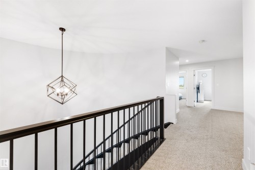 Upper-level landing featuring a geometric pendant light, dark wood-finish handrail, and light-colored carpeting - 3193 Checknita Way, Edmonton, AB - Indoor Photo Showing Other Room