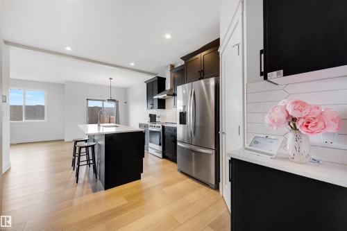 Open-concept kitchen featuring an island with a breakfast bar, stainless steel appliances, dark cabinetry, and light wood-finish flooring - 3193 Checknita Way, Edmonton, AB - Indoor Photo Showing Kitchen With Stainless Steel Kitchen With Upgraded Kitchen