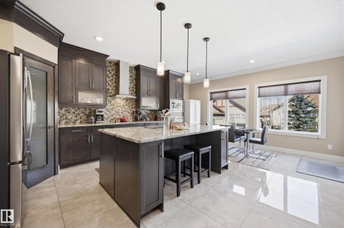 A spacious kitchen featuring dark wood cabinetry, granite countertops, and a tiled backsplash - 2018 Armitage Green, Edmonton, AB - Indoor Photo Showing Kitchen With Upgraded Kitchen