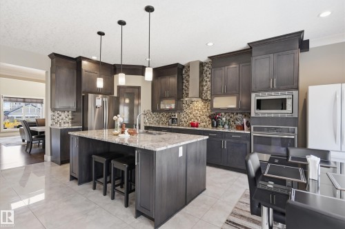 The kitchen features dark wood cabinetry, a central island with a granite countertop, and stainless steel appliances - 2018 Armitage Green, Edmonton, AB - Indoor Photo Showing Kitchen With Upgraded Kitchen