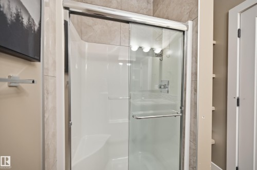 Bathroom featuring a shower with a clear glass sliding door and chrome hardware, and tiled walls - 2018 Armitage Green, Edmonton, AB - Indoor Photo Showing Bathroom