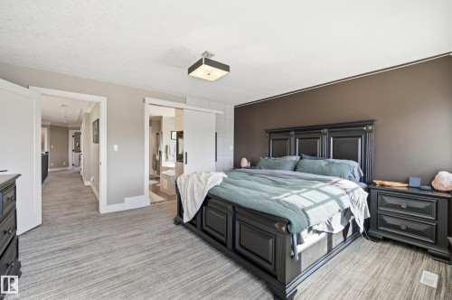 This bedroom features a dark wooden bed frame and matching nightstands, a neutral-toned accent wall, and light-colored carpeting - 2018 Armitage Green, Edmonton, AB - Indoor Photo Showing Bedroom