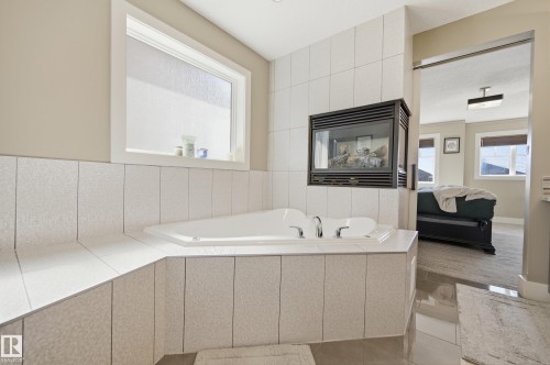 Bathroom featuring a built-in bathtub with chrome fixtures, a window above the tub, and a wall-mounted fireplace - 2018 Armitage Green, Edmonton, AB - Indoor Photo Showing Bathroom