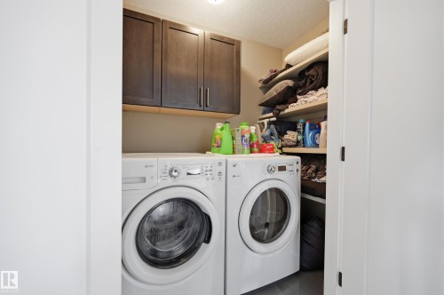 Practical laundry area featuring a front-load washer and dryer, dark wood cabinetry, and open shelving for additional storage - 2018 Armitage Green, Edmonton, AB - Indoor Photo Showing Laundry Room