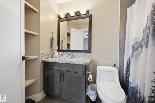 Bathroom featuring a dark wood vanity with a granite countertop and a tile backsplash, a mirror with an overhead light fixture, and built-in shelving - 2018 Armitage Green, Edmonton, AB - Indoor Photo Showing Bathroom