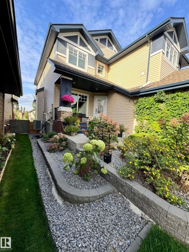 The property exterior features two stories, a front entrance with a decorative glass door, and a landscaped front yard with a gravel path, lawn, and various plantings - 2018 Armitage Green, Edmonton, AB - Outdoor