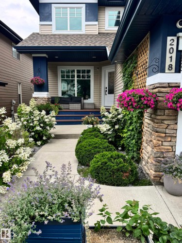 The property features a welcoming entrance with a stone-clad pillar, a light-colored exterior siding, and a contrasting dark blue trim - 2018 Armitage Green, Edmonton, AB - Outdoor With Deck Patio Veranda