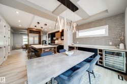 Contemporary dining space featuring a concrete-finish table, linear pendant lighting, built-in dry bar with a wine refrigerator, a stone-finish accent wall, and light wood-finish flooring - 