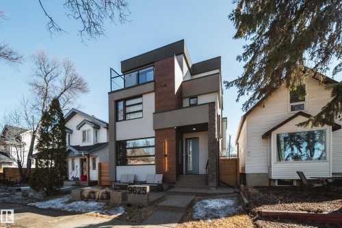 Contemporary multi-level exterior featuring varied cladding, a prominent flat roofline, an upper-level balcony with glass railing, an integrated front entry with stone-clad pillars, and a light blue entry door - 9625 101 Street, Edmonton, AB - Outdoor With Facade
