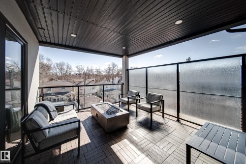 Covered outdoor balcony featuring wood-finish flooring, a metal ceiling with recessed lighting, and a glass-paneled railing - 9625 101 Street, Edmonton, AB - Outdoor With Deck Patio Veranda With Exterior