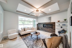 Spacious living area featuring a contemporary linear fireplace with a textured wood-look surround, light-finish flooring, and a detailed coffered ceiling with recessed lighting - 