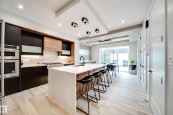 Contemporary kitchen featuring a waterfall island with a quartz countertop, black cabinetry, stainless steel appliances, and wood-finish flooring - 