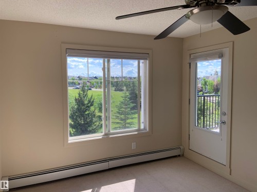 Interior space featuring a window with expansive outdoor views, a glass-paneled door opening to a balcony, a ceiling fan with integrated lighting, and baseboard heating - 307 6084 Stanton Drive, Edmonton, AB - Indoor Photo Showing Other Room