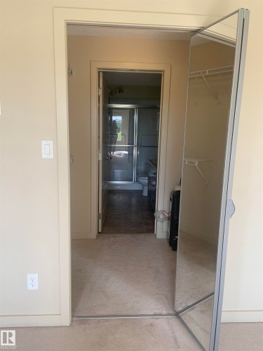 Mirrored closet door with interior shelving, carpeted flooring, and a doorway leading to a bathroom featuring a glass-enclosed shower and tiled flooring - 307 6084 Stanton Drive, Edmonton, AB -  Photo Showing Other Room