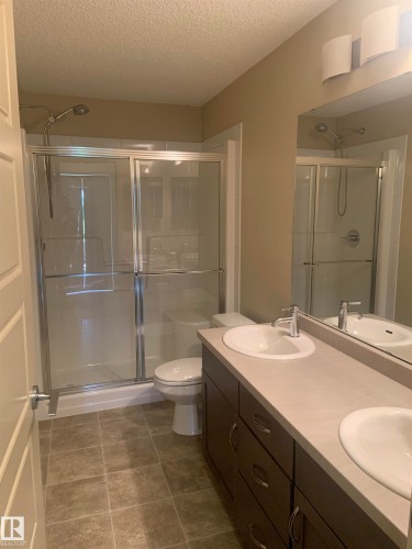 Bathroom featuring a dual vanity with undermount sinks, a light-toned countertop, and dark wood-finish cabinetry - 307 6084 Stanton Drive, Edmonton, AB - Indoor Photo Showing Bathroom