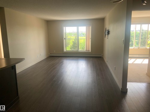 Spacious living area featuring dark wood-finish flooring, neutral wall paint, and a large sliding glass door leading to a balcony - 307 6084 Stanton Drive, Edmonton, AB - Indoor Photo Showing Other Room