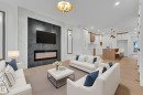 Open-concept living area with a contemporary electric fireplace, light wood-finish flooring, recessed lighting, and a modern kitchen featuring white and wood-finish cabinetry - 456 Crystal Creek Link, Leduc, AB  - Indoor Photo Showing Living Room With Fireplace 