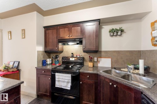 The property features a kitchen with dark wood cabinetry, a black electric range, and a double basin stainless steel sink - #211 4415 48 St, Leduc, AB - Indoor Photo Showing Kitchen With Double Sink