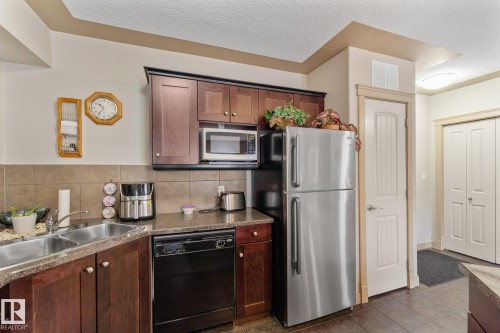 The kitchen features wooden cabinetry, a double basin sink, and a stainless steel refrigerator - #211 4415 48 St, Leduc, AB - Indoor Photo Showing Kitchen With Double Sink