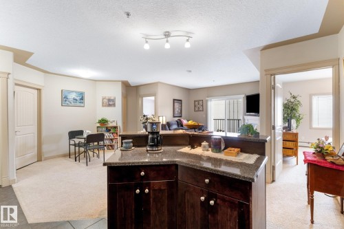The kitchen features dark wood cabinetry and granite countertops, with a view of the living area and access to the balcony - #211 4415 48 St, Leduc, AB - Indoor