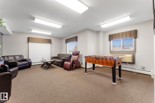 The recreation room features carpet flooring, ample overhead lighting, and windows with blinds - #211 4415 48 St, Leduc, AB - Indoor