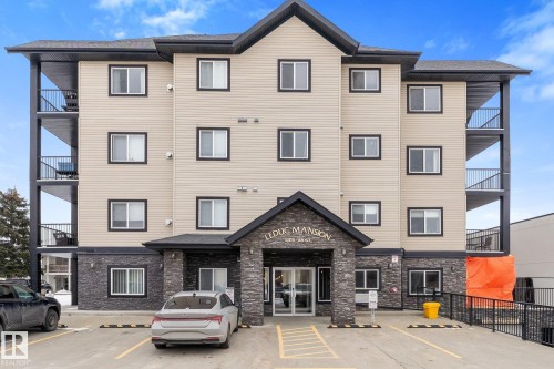 The property features a multi-story building with a light-colored facade and dark trim around the windows - #211 4415 48 St, Leduc, AB - Outdoor