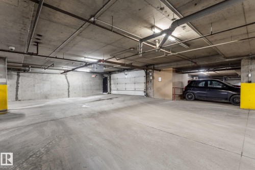 The property features an underground parking area with concrete walls and flooring, and exposed piping on the ceiling - #211 4415 48 St, Leduc, AB - Indoor Photo Showing Garage