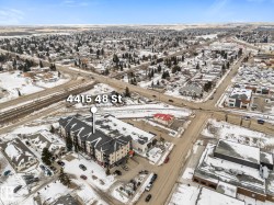 Aerial view of the property and surrounding neighborhood, featuring a large apartment building with a dark roof and light-colored facade - 