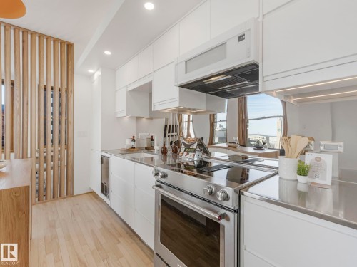 Modern kitchen featuring light hardwood flooring, white cabinetry, stainless steel appliances, and a wooden slatted room divider - 807 10134 100 Street, Edmonton, AB - Indoor Photo Showing Kitchen With Upgraded Kitchen