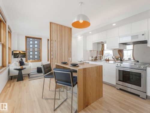 The kitchen features white cabinetry, stainless steel appliances, and a light wood island with seating - 807 10134 100 Street, Edmonton, AB - Indoor Photo Showing Kitchen
