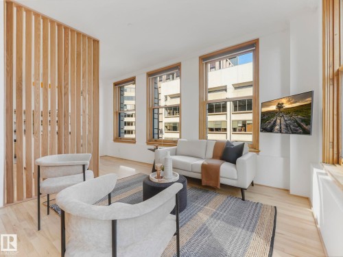 The property features light-colored hardwood flooring throughout, tall windows with wooden frames, and a wooden slatted partition - 807 10134 100 Street, Edmonton, AB - Indoor Photo Showing Living Room