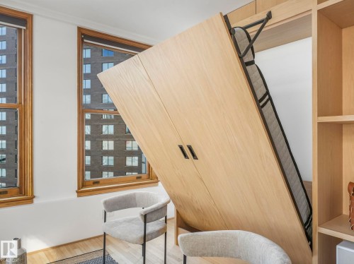 This room features two windows with wooden frames, hardwood flooring, and a built-in wooden wall unit with shelving and a hideaway bed - 807 10134 100 Street, Edmonton, AB - Indoor Photo Showing Other Room