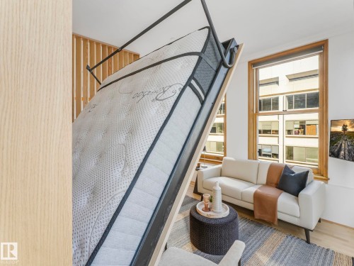 This versatile space features a convenient wall bed system, a two-seater sofa, and large windows with wooden frames - 807 10134 100 Street, Edmonton, AB - Indoor