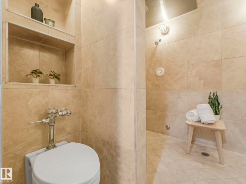 Bathroom featuring light-colored wall tiles, a built-in shower with a rainfall showerhead, and a toilet with a chrome flushometer - 807 10134 100 Street, Edmonton, AB - Indoor Photo Showing Bathroom