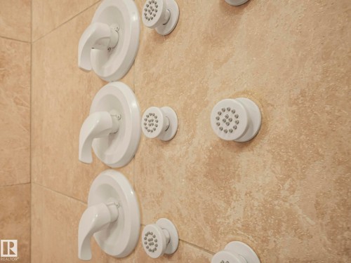 Shower wall with beige stone tiling and a full system of shower controls and body jets - 807 10134 100 Street, Edmonton, AB - Indoor Photo Showing Bathroom