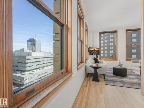 The property offers a living space featuring light hardwood flooring and multiple windows with wooden frames - 807 10134 100 Street, Edmonton, AB - Indoor Photo Showing Other Room