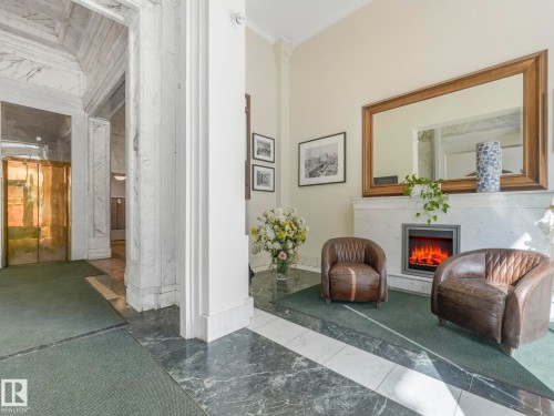 The property features a lobby with marble flooring and walls, an ornate gold elevator, and a fireplace with an electric insert - 807 10134 100 Street, Edmonton, AB - Indoor Photo Showing Other Room