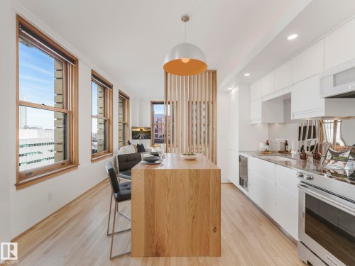 This inviting space showcases light wood flooring, a contemporary kitchen with white cabinetry and stainless steel appliances, and a unique wood slat partition - 807 10134 100 Street, Edmonton, AB - Indoor Photo Showing Kitchen
