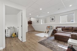 Finished lower level featuring recessed lighting, wood-finish flooring, two windows with blinds, a white drop ceiling, and a carpeted staircase - 