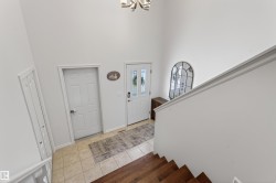 Grand foyer featuring an entry door with decorative glass, a high ceiling, tile flooring, wood-finish stairs, and a built-in closet - 
