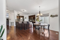 Spacious kitchen and dining area featuring rich wood-finish flooring, dark wood cabinetry, a breakfast bar, and stainless steel appliances - 